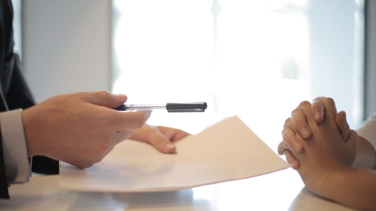 An adviser hands a document and a pen to a client across a negotiation table